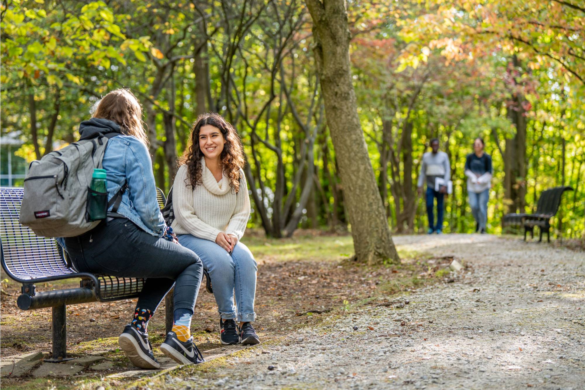 Students in a park sitting on a bench talking with people walking in the background
